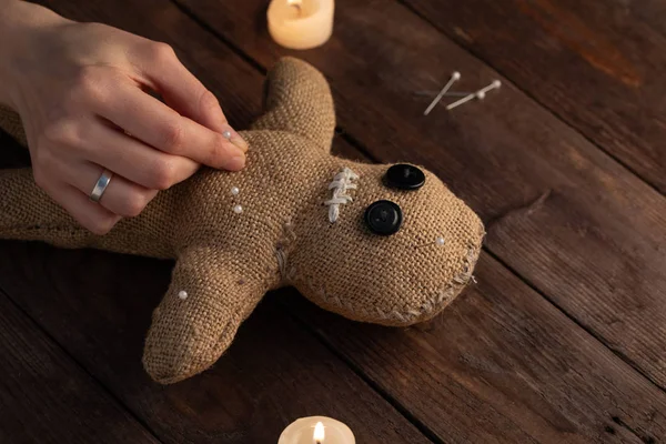 Muñeca vudú sobre fondo de madera con iluminación dramática y velas. El concepto de brujería y arte negro. Muñeca de arpillera sobre fondo de madera. Las manos clavan alfileres en una muñeca. Copiar espacio . —  Fotos de Stock