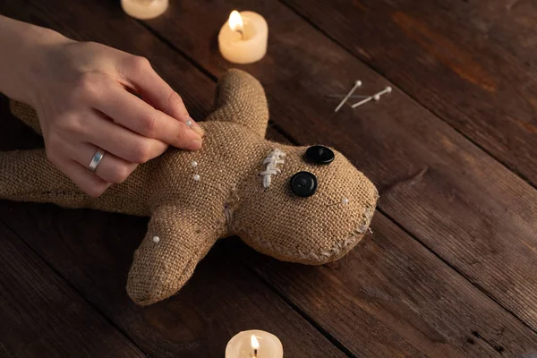 Muñeca vudú sobre fondo de madera con iluminación dramática y velas. El concepto de brujería y arte negro. Muñeca de arpillera sobre fondo de madera. Las manos clavan alfileres en una muñeca. Copiar espacio . —  Fotos de Stock