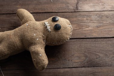 Voodoo doll on a wooden background with dramatic lighting. The concept of witchcraft and black art. Burlap doll on a wooden background. Pierce with maces. Copy space.