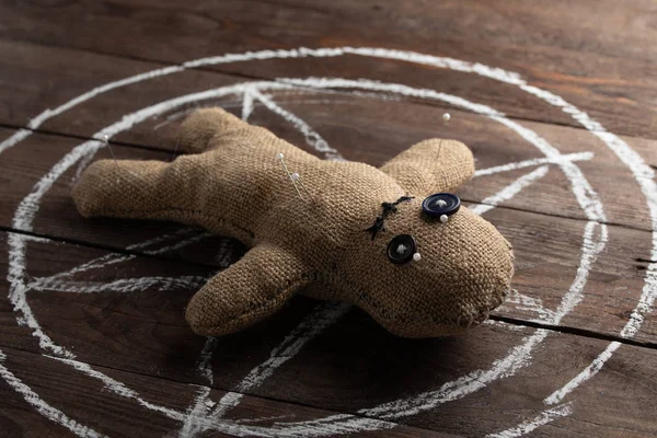 Voodoo pop op een houten achtergrond met dramatische verlichting. Het concept van hekserij en zwarte kunst en het occulte. Burlap pop op de achtergrond van een getekende ster. Stuck pinnen in de pop. — Stockfoto