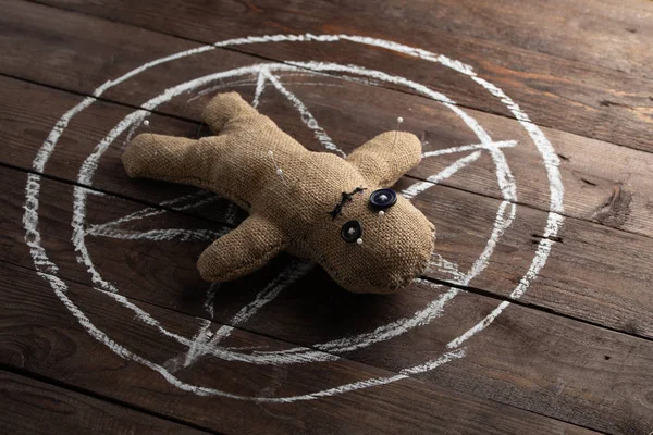 Voodoo baba fából készült háttérrel, drámai megvilágítással. A boszorkányság, a fekete művészet és az okkultizmus fogalma. Egy vászonbaba egy rajzolt csillag hátterében. Tűkkel a babában.. — Stock Fotó