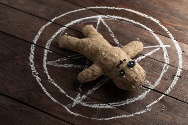 Muñeca vudú sobre fondo de madera con iluminación dramática. El concepto de brujería y arte negro y lo oculto. Muñeca de arpillera en el fondo de una estrella dibujada. Alfileres atascados en la muñeca . —  Fotos de Stock