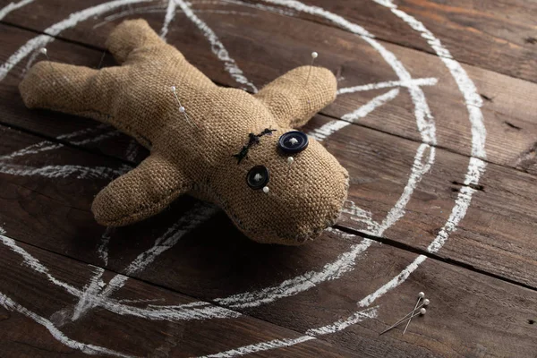Voodoo baba fából készült háttérrel, drámai megvilágítással. A boszorkányság, a fekete művészet és az okkultizmus fogalma. Egy vászonbaba egy rajzolt csillag hátterében. Tűkkel a babában.. — Stock Fotó