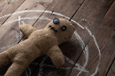 Tahta arka planda dramatik ışıklandırmalı bir vudu bebeği. Büyücülük, kara sanat ve okült kavramı. Çizilmiş bir yıldızın arka planındaki çuval bezi bebek. Oyuncak bebeğe iğneler saplanmış..