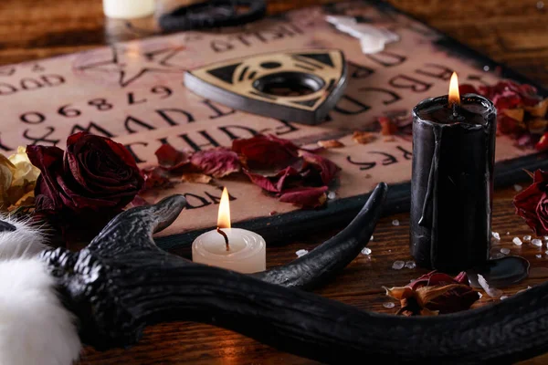 Tabla de diálogo y plancheta, también conocida como tabla Ouija, utilizada para comunicarse con los muertos y otros espíritus. La atmósfera del arte negro con velas y cuernos del animal . —  Fotos de Stock