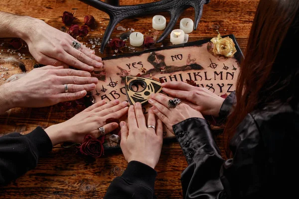 Personas que llevan a cabo una sesión de espiritismo usando una Ouija Board, o Talking Spirit Board, con velas blancas. Disparo desde arriba . —  Fotos de Stock