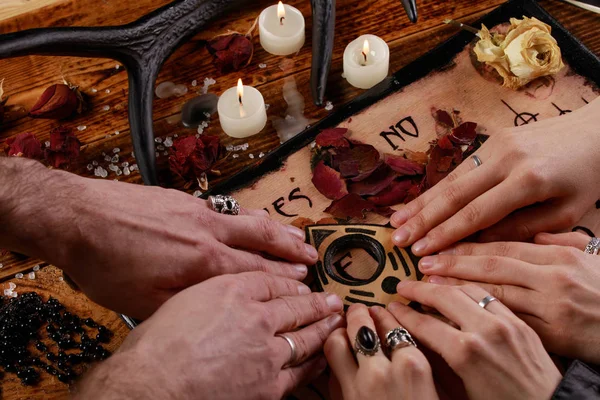 Människor som utför en seans med hjälp av en Ouija Board, eller Talking Spirit Board, med vita ljus. Skjuten från ovan. — Stockfoto
