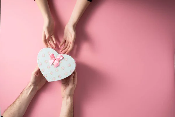 Valentijnsdag viering concept. Een mooi cadeau van een geliefde. Doos met een boog handen van een man en een vrouw op een delicate roze achtergrond. Begrepen, ruimte. Vlakke plaat. — Stockfoto