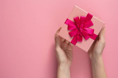 Sevgililer Günü kutlaması konsepti. Sevdiğin birinden güzel bir hediye. Zarif pembe bir arka planda, kadın ellerinde bir fiyonk olan bir kutu. Uzayı kopyala Düz yatıyordu.