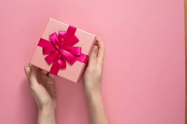 バレンタインデーのお祝いのコンセプト。愛する人からの素敵な贈り物。繊細なピンクの背景に女性の手で弓とボックス。コピースペース平敷. — ストック写真