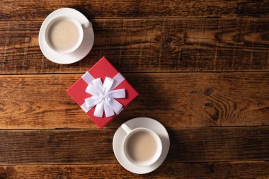 Valentine's Day celebration concept. A nice gift for your loved one. Hands of man and woman with coffee mugs on a wooden table background. Copy space.
