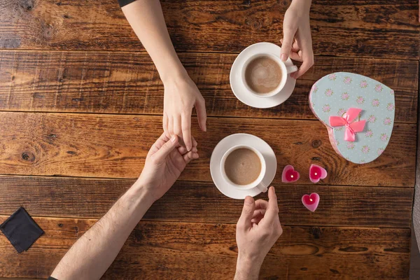 Valentine's Day celebration concept. A nice gift for your loved one. Hands of man and woman with coffee mugs on a wooden table background. Copy space. Flat lay. Close-up. — 스톡 사진