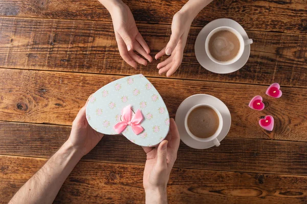 Valentine's Day celebration concept. A nice gift for your loved one. Hands of man and woman with coffee mugs on a wooden table background. Copy space. Flat lay. Close-up. — 스톡 사진