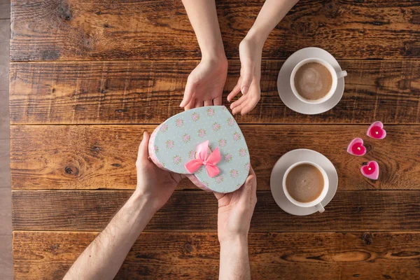 Valentine's Day celebration concept. A nice gift for your loved one. Hands of man and woman with coffee mugs on a wooden table background. Copy space. Flat lay. Close-up. — 스톡 사진