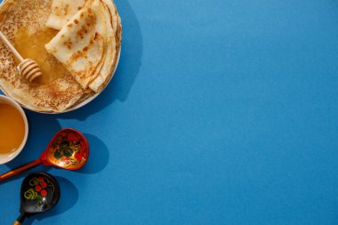 Mavi arka planda ballı lezzetli ev yapımı krepler. Üst manzara, yakın plan. Geleneksel tatil kutlaması konsepti. Rusça çeviri geniş ve mutlu Maslenitsa.