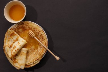 Siyah arka planda ballı nefis ev yapımı krepler. Üst manzara, yakın plan. Geleneksel tatil kutlaması konsepti. Rusça çeviri geniş ve mutlu Maslenitsa.