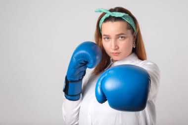 Kız gücü konsepti. Kendine güvenen genç bir kadın gri bir duvar arkasında izole edilmiş. Kadın ve bağımsız güç. Kız vurmak için boks eldiveniyle elini kaldırdı. Stüdyo çekimi.