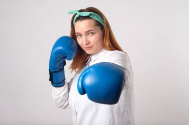 Kız gücü konsepti. Kendine güvenen genç bir kadın gri bir duvar arkasında izole edilmiş. Kadın ve bağımsız güç. Kız vurmak için boks eldiveniyle elini kaldırdı. Stüdyo çekimi.