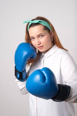 Kız gücü konsepti. Kendine güvenen genç bir kadın gri bir duvar arkasında izole edilmiş. Kadın ve bağımsız güç. Kız vurmak için boks eldiveniyle elini kaldırdı. Stüdyo çekimi.
