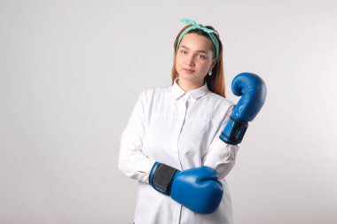 Kız gücü konsepti. Gri duvar arkasında izole edilmiş kendine güvenen genç bir kadın. Kadınsı ve bağımsız güç. Boks eldivenli kız. Kadın gücü konsepti. Bir kıza boks eldiveni giydirmek. Yakın plan..