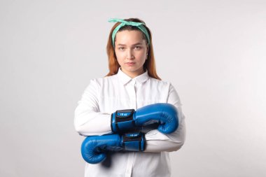 Kız gücü konsepti. Gri duvar arkasında izole edilmiş kendine güvenen genç bir kadın. Kadınsı ve bağımsız güç. Boks eldivenli kız. Kadın gücü konsepti. Bir kıza boks eldiveni giydirmek. Yakın plan..
