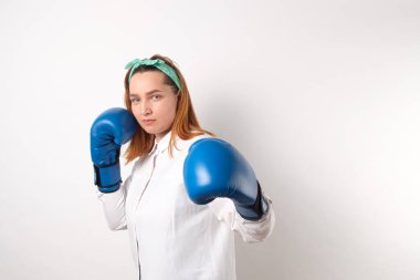 Kız gücü konsepti. Kendine güvenen genç bir kadın gri bir duvar arkasında izole edilmiş. Kadın ve bağımsız güç. Kız vurmak için boks eldiveniyle elini kaldırdı. Stüdyo çekimi.