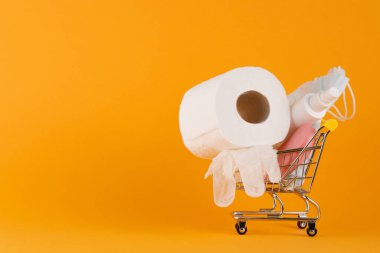 Tıbbi maske ve dezenfeksiyon eldivenleri sarı arka planda alışveriş arabasında. Virüs koruma konsepti. Virüsün yayılmasını önlemek ve salgın COVID-19.