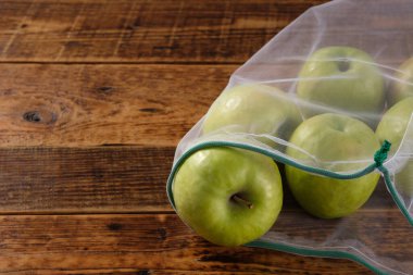 Sıfır atık, plastiksiz geri dönüştürülmüş tekstil meyve elma veya sebze taşımak için poşet, ahşap bir yüzey. Tekrar kullanılabilir. Boşluğu kopyala.