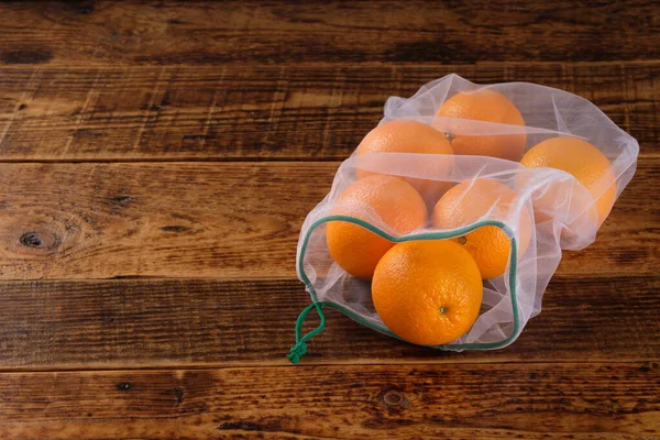 Zero waste, plastic free recycled textile produce bag for carrying fruit orange or vegetables, a wooden surface. Reusable using. Copy space.