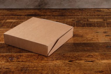 Tahta arka planda izole edilmiş büyük kahverengi karton kutu. Çevre dostu tek kullanımlık yiyecek ambalajı. Doğa ve geri dönüşüm kavramının korunması.