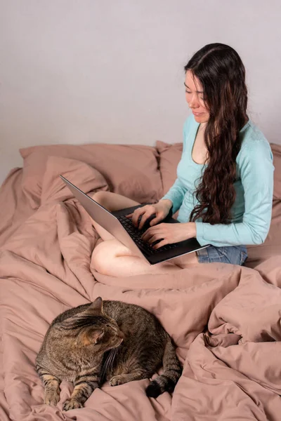 The concept of social distance and isolation. Work from home remotely over the Internet. A young woman works at home on a computer and a cat is next to her. Quarantine. Copy space.