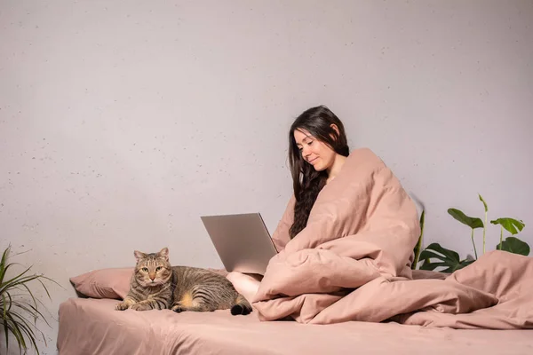 The concept of social distance and isolation. Work from home remotely over the Internet. A young woman works at home on a computer and a cat is next to her. Quarantine. Copy space.