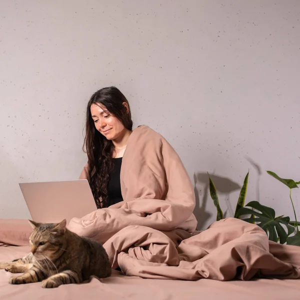 The concept of social distance and isolation. Work from home remotely over the Internet. A young woman works at home on a computer and a cat is next to her. Quarantine.