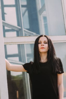 Kısacası küçük elbise mavi cam arka plan üzerinde siyah poz genç sıska çekici güzel ve seksi esmer kadın hanım. soğuk renkler, yüksek moda