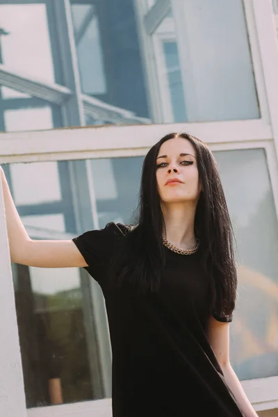 Junge schlanke, charmante und sexy brünette Frau, die in einem kurzen, kleinen schwarzen Kleid auf blauem Glashintergrund posiert. kalte Farben, hohe Mode — Stockfoto