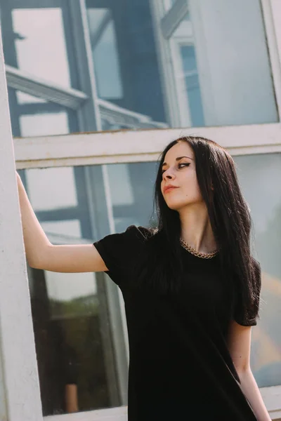 Junge schlanke, charmante und sexy brünette Frau, die in einem kurzen, kleinen schwarzen Kleid auf blauem Glashintergrund posiert. kalte Farben, hohe Mode — Stockfoto