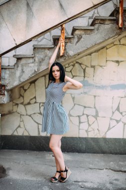 Genç sıska kısa elbise siyah ve beyaz çizgili poz Bayan büyüleyici. güzel ve seksi esmer gösteren moda poz terk edilmiş binalar arka plan üzerinde