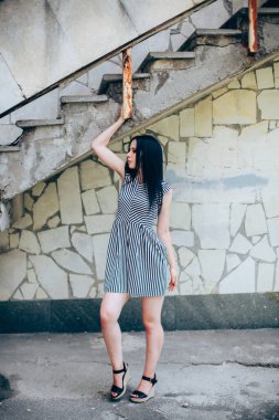 Genç sıska kısa elbise siyah ve beyaz çizgili poz Bayan büyüleyici. güzel ve seksi esmer gösteren moda poz terk edilmiş binalar arka plan üzerinde