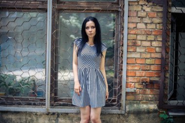 Genç sıska kısa elbise siyah ve beyaz çizgili poz Bayan büyüleyici. güzel ve seksi esmer gösteren moda poz terk edilmiş binalar arka plan üzerinde