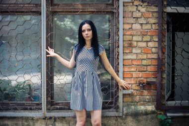 Genç sıska kısa elbise siyah ve beyaz çizgili poz Bayan büyüleyici. güzel ve seksi esmer gösteren moda poz terk edilmiş binalar arka plan üzerinde