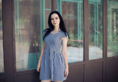 Genç sıska kısa elbise siyah ve beyaz çizgili poz Bayan büyüleyici. güzel ve seksi esmer gösteren moda poz terk edilmiş binalar arka plan üzerinde