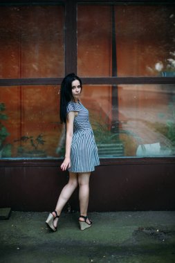 Genç sıska kısa elbise siyah ve beyaz çizgili poz Bayan büyüleyici. güzel ve seksi esmer gösteren moda poz terk edilmiş binalar arka plan üzerinde