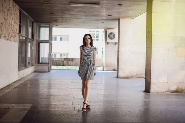 Fiatal vékony magas nő pózol a rövid ruha csíkokkal. bájos és szexi barna divat jelent jeleníti meg a háttérben, az elhagyott épületek. — Stock Fotó