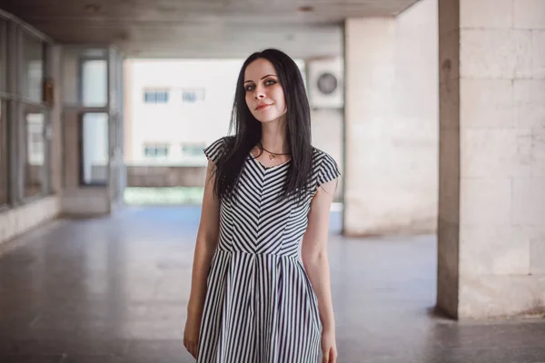 Junge schlanke, große Frau, die in einem kurzen Kleid mit Streifen posiert. Charmant und sexy Brünette zeigt Mode Pose auf dem Hintergrund der verlassenen Gebäude. — Stockfoto