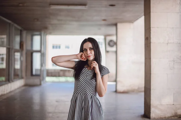 young skinny tall woman posing in short dress with stripes. charming and sexy brunette shows fashion pose on the background of the abandoned buildings.