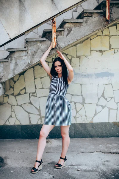 Junge schlanke, charmante Dame posiert in einem kurzen schwarzen und weißen Kleid mit Streifen. schöne und sexy Brünette demonstriert Mode-Pose auf dem Hintergrund der verlassenen Gebäude — Stockfoto