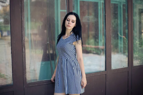 Junge schlanke, charmante Dame posiert in einem kurzen schwarzen und weißen Kleid mit Streifen. schöne und sexy Brünette demonstriert Mode-Pose auf dem Hintergrund der verlassenen Gebäude — Stockfoto