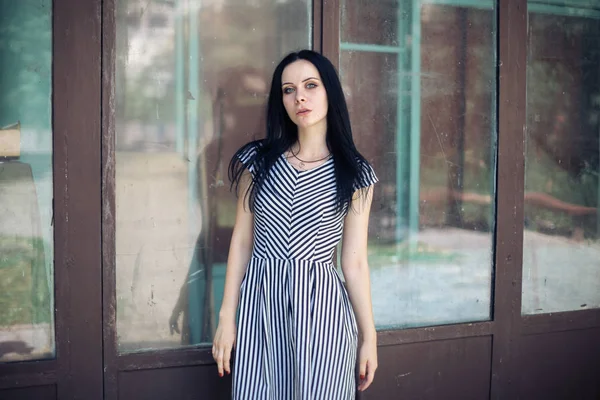 young skinny charming lady posing in short dress black and white with stripes. nice and sexy brunette demonstrating fashion pose on the background of the abandoned buildings