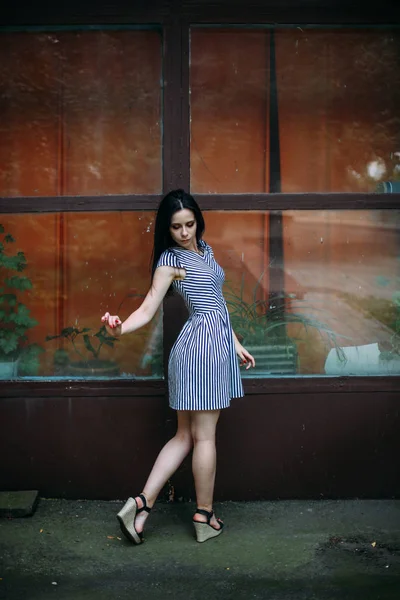 Junge schlanke, charmante Dame posiert in einem kurzen schwarzen und weißen Kleid mit Streifen. schöne und sexy Brünette demonstriert Mode-Pose auf dem Hintergrund der verlassenen Gebäude — Stockfoto
