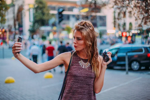 Uroczy młoda dziewczyna blond Dokonywanie selfie. sexy. idealne, profesjonalne włosy i makijaż. retusz, Selektywny fokus. pozowanie. Wieczorem miasto światła na tle — Zdjęcie stockowe